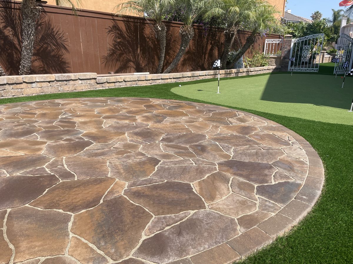 Circular flagstone patio beside a putting green with a stone seat wall