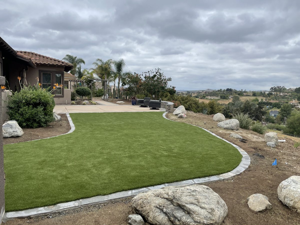 Artificial turf lawn edged with a stone border by Catalina Hardscapes